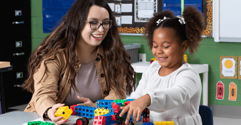Young female teacher working with a young female student on interactive blocks. Both are smiling.
