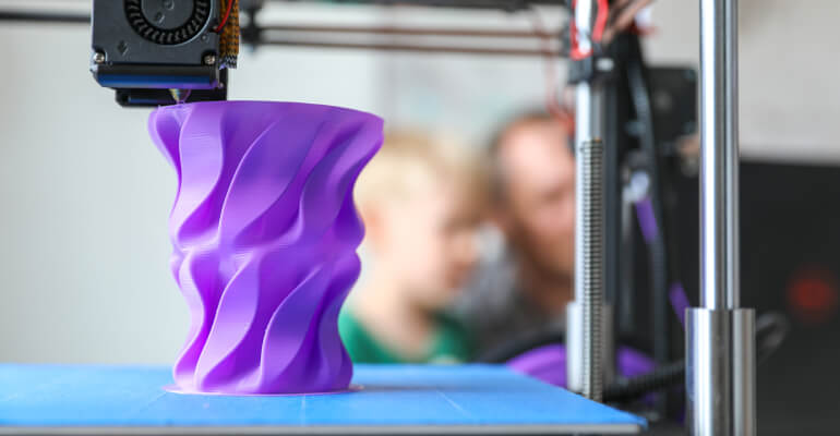 A 3D printer creates a purple vase-like object.
