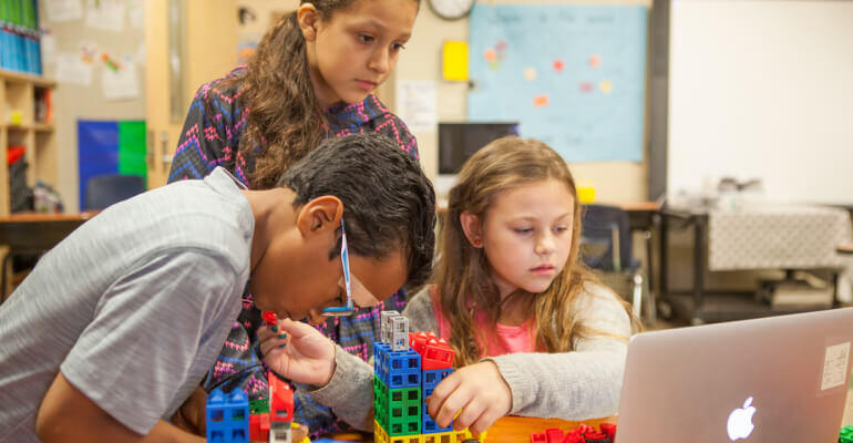 Group of three students sitting around a laptop and working on a block-based STEM lesson on coding