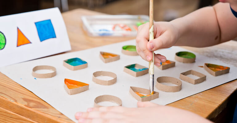 Close up of a child's hands working on painting different shapes with the help of stencils
