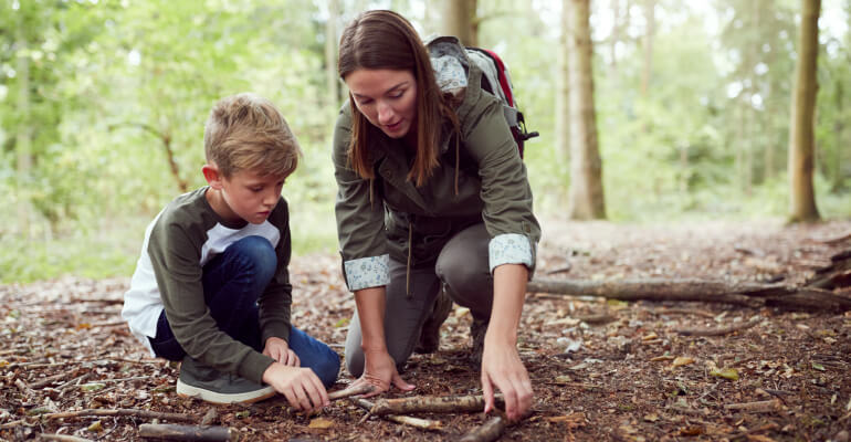 Male student and female teacher out on a nature walk. They are kneeling down on a mulched area and examining something on the ground.