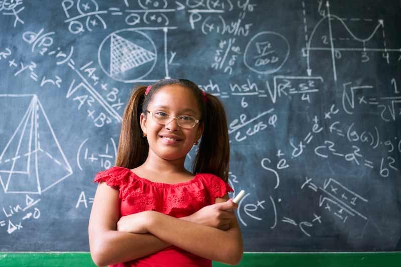 young girl standing in front of blackboard covered in mathematical formulas