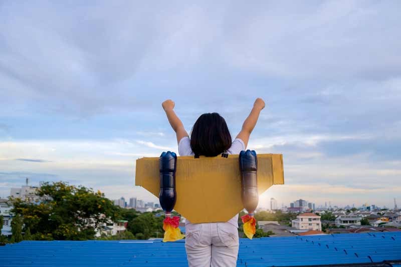 image of an inspired young girl with a cardboard jetpack on her back looking out over a city